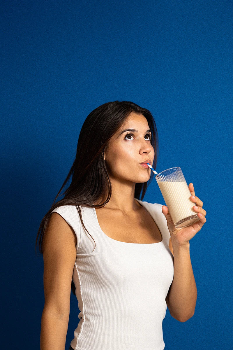 Woman drinking a milkshake against a blue background