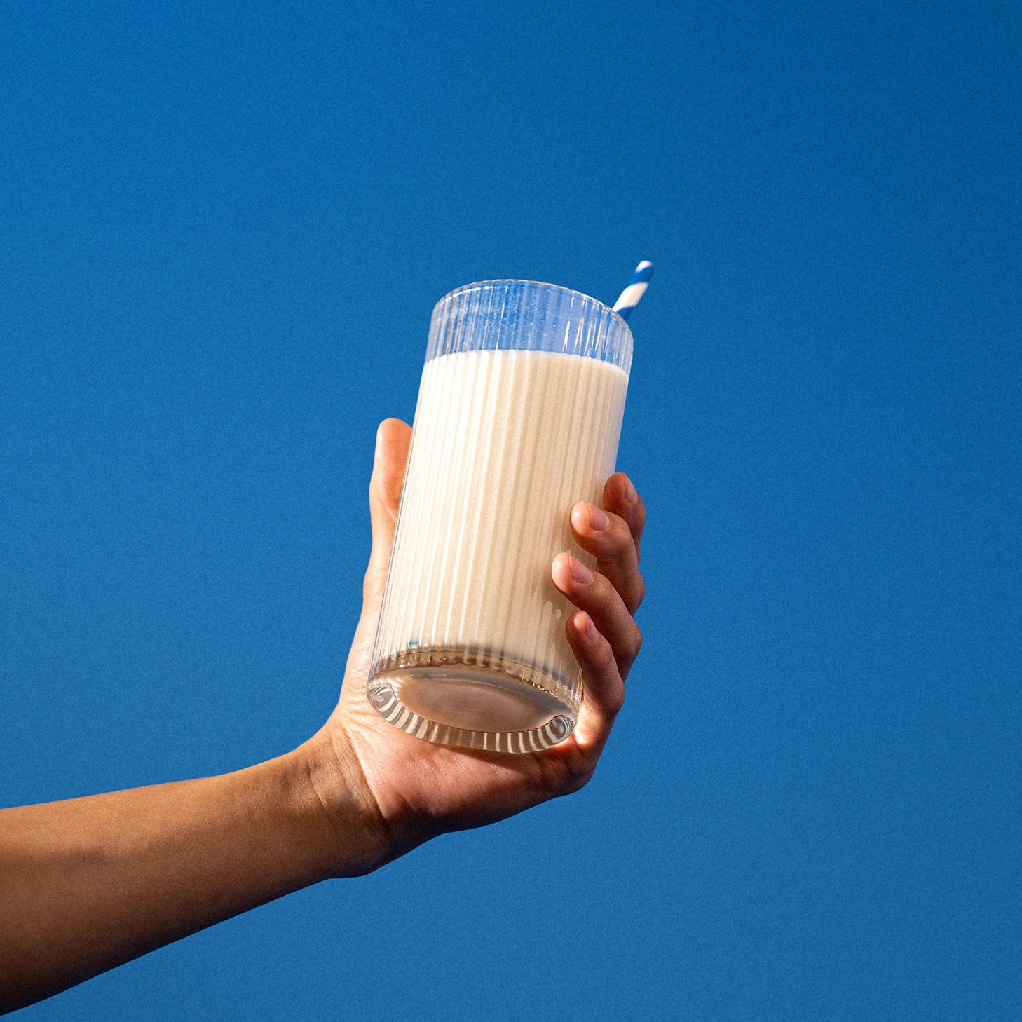 Hand holding a glass of milk against a blue background